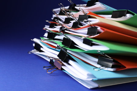 Many folders with documents and binder clips on blue background, closeupの写真素材