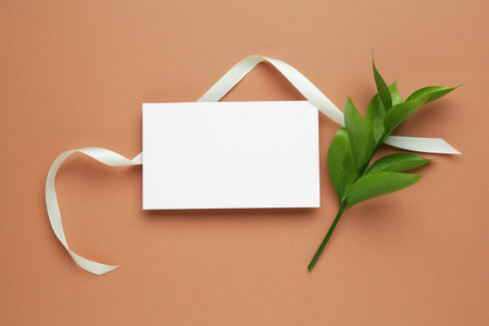Blank card and green leaves on beige background, flat layの写真素材