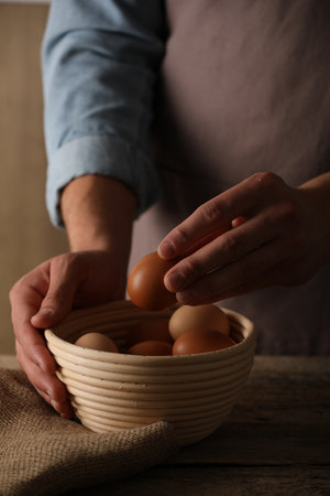 Person putting raw chicken egg into bowl at wooden table, closeupの写真素材