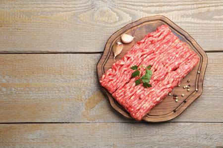 Raw minced meat with parsley and spices on wooden table, top view. Space for text
