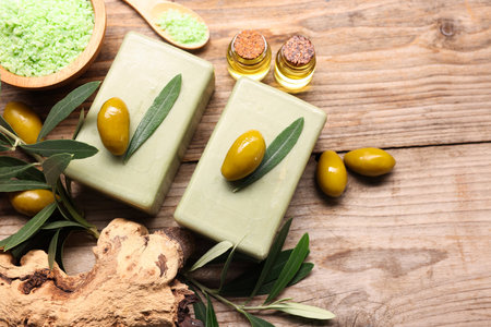 Handmade soap bars, olives, sea salt, essential oils and green leaves on wooden table, flat lay. Space for textの写真素材