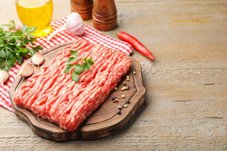 Raw minced meat with parsley and spices on wooden table, closeup. Space for text