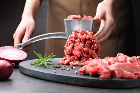 Woman making minced meat with grinder at gray table, closeupの写真素材