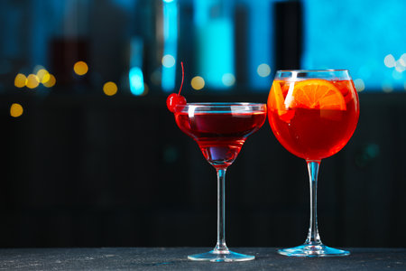 Glasses of tasty cocktails on dark table against blurred background, bokeh effect.の写真素材