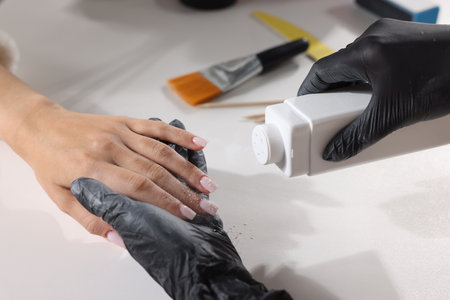 Woman sprinkling talcum powder on client's hand after manicure procedure at table in salon, closeupの写真素材