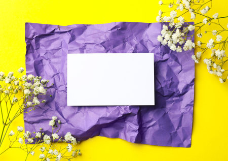 Blank card and beautiful flowers on yellow background, flat lay