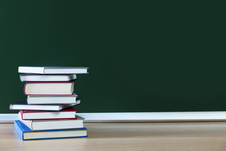 Happy Teacher's Day. Stack of books on wooden table near chalkboard, space for text