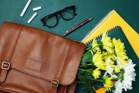 Happy Teacher's Day. Notebooks, flowers, bag and pieces of chalk on chalkboard, flat layの写真素材