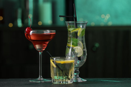 Glasses of tasty cocktails on dark table against blurred background, bokeh effect
