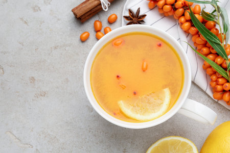 Sea buckthorn tea in cup, spices, lemon and fresh berries on light gray table, flat lay. Space for textの写真素材