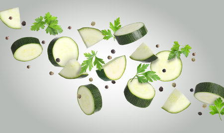 Fresh zucchini pieces and parsley falling against gray backgroundの写真素材
