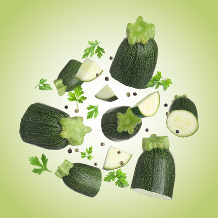 Fresh zucchini pieces and parsley falling against light green backgroundの写真素材