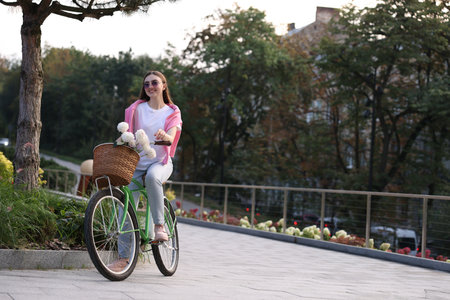 Woman riding bicycle with flowers in basket on city street. Space for textの写真素材