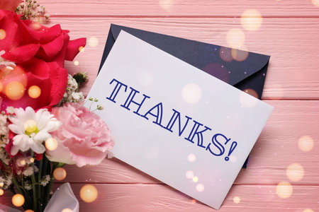 Thank you card, envelope and flowers on pink wooden background, top view. Bokeh lights
