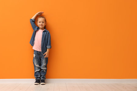 Little girl measuring her height near orange wall indoors, space for textの写真素材