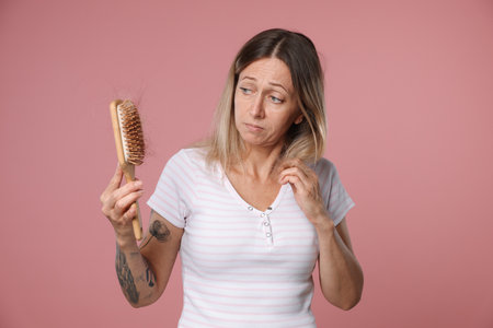 Alopecia problem. Sad woman holding brush with lost hair on pink backgroundの写真素材