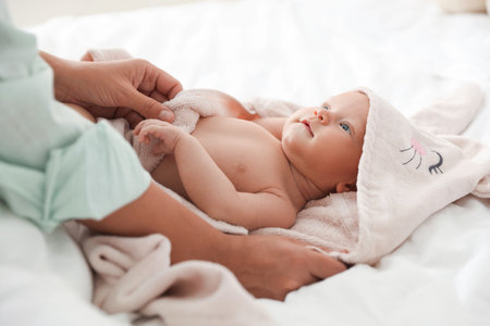 Mother covering her baby with towel after bathing on bed, closeup