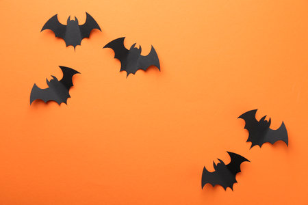 Halloween decor. Black paper bats on orange background, flat lay. Space for textの写真素材