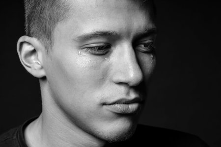 Sad man crying on dark background, closeup. Black and white effect