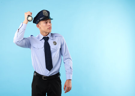 Young policeman in uniform with flashlight on light blue background, space for textの写真素材