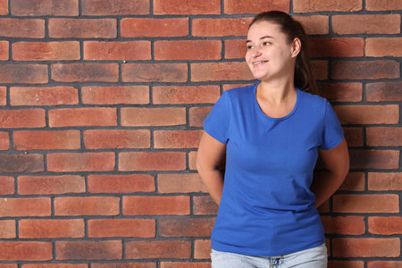Young woman wearing stylish blue t-shirt near brick wall. Mockup for designの写真素材