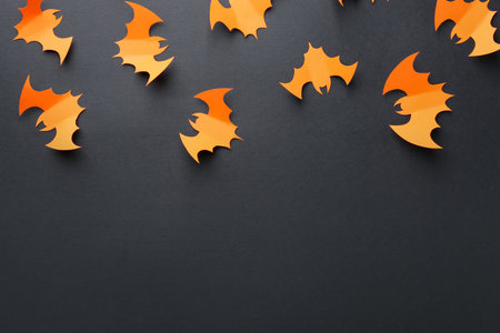 Halloween decor. Orange paper bats on black background, flat lay. Space for textの写真素材
