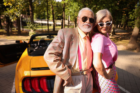 Stylish senior couple in sunglasses near modern cabriolet outdoors