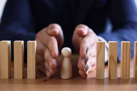 Risk. Man stopping domino effect to protect wooden figure at table, closeupの写真素材
