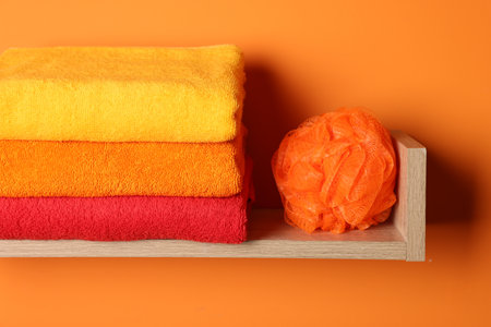 Stack of fresh towels and sponge on shelf on orange wall, closeupの写真素材