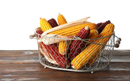 Red and yellow corn cobs in basket on wooden table against white background