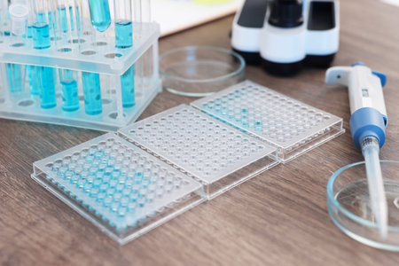 Research in genetics. Microplates with samples, test tubes and micropipette on wooden table, closeup