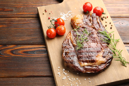 Delicious grilled beef steak with herbs, spices and tomatoes on wooden table, closeup. Space for textの写真素材