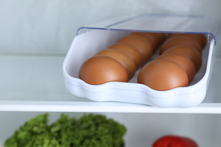 Container with raw chicken eggs on shelf in refrigerator, closeupの写真素材