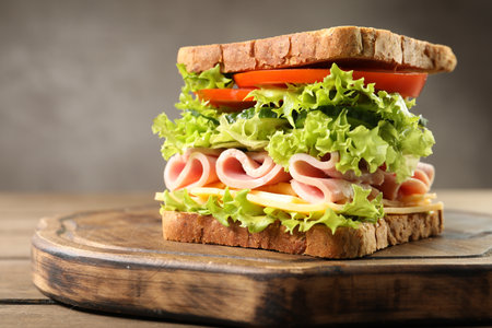 Tasty sandwich with ham, cheese and vegetables on wooden table, closeupの写真素材