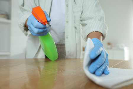 Woman spraying cleaning product while wiping wooden table with rag at home, closeupの写真素材