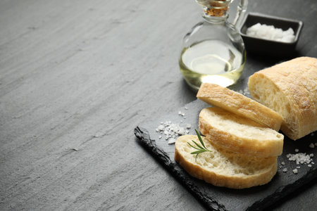 Cut crispy ciabatta, rosemary, salt and oil on black textured table, closeup. Space for textの写真素材