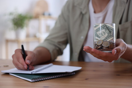 Man with glass jar of money budgeting at wooden desk, selective focusの写真素材