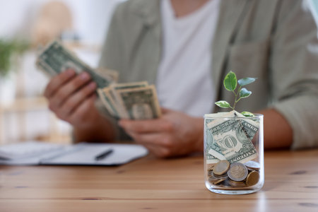 Glass jar with money and seedling. Man budgeting at desk, selective focusの写真素材