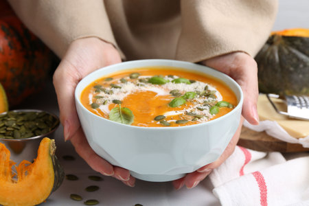 Woman with bowl of delicious pumpkin soup at table, closeupの写真素材