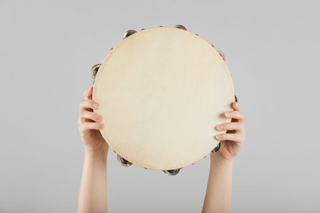 Woman playing tambourine on light background, closeup