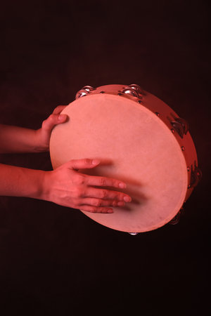 Woman playing tambourine in color light on black background with smoke, closeupの写真素材