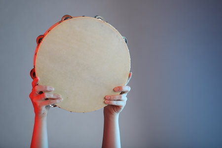 Woman playing tambourine on gray background, closeup. Space for textの写真素材