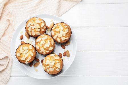 Tasty muffins with almond flakes and nuts on white wooden table, top view. Space for textの写真素材