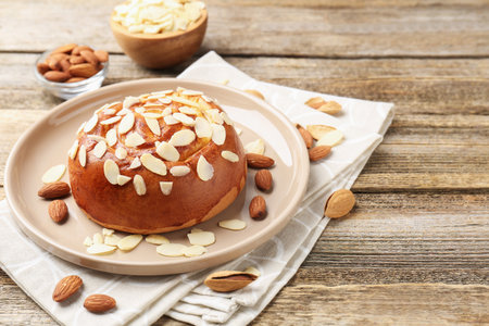 Tasty roll bun with almond flakes and nuts on wooden table, closeup. Space for textの写真素材