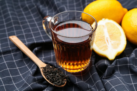 Aromatic black tea in glass cup, dried leaves and lemons on tablecloth, closeupの写真素材
