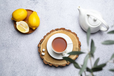 Aromatic black tea in cup, sugar, lemons and teapot on light gray table, flat layの写真素材