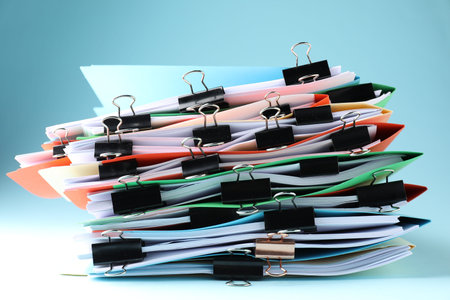 Many folders with documents and binder clips on light blue background, closeup