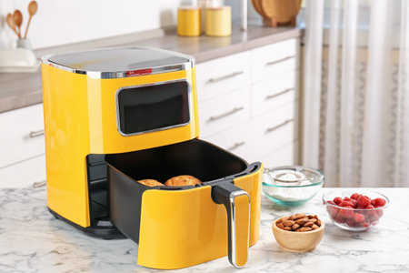 Air fryer with baked muffins and ingredients on white marble table in kitchen, closeupの写真素材
