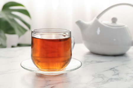 Aromatic black tea in glass cup and teapot on white marble table, closeup. Space for textの写真素材