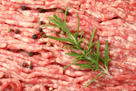 Raw minced meat with peppercorns and rosemary as background, top viewの写真素材